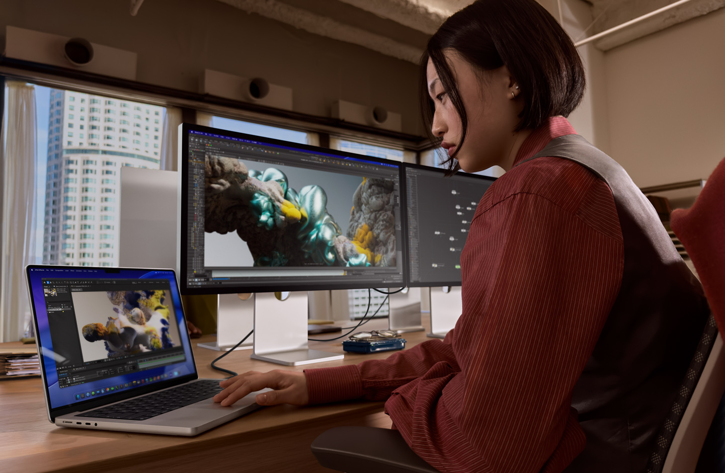Člověk v kanceláři pracuje na MacBooku, ke kterému je přes port Thunderbolt 5 připojený Studio Display XDR