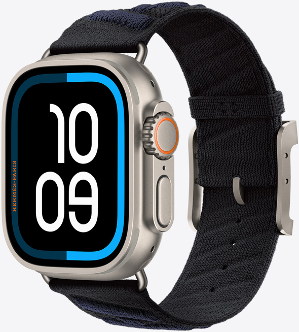 Apple Watch Hermès Ultra 3, titanium case, natural colour, edge-to-edge display, rounded corners, right side exterior, Digital Crown, microphone, raised side button, digital watch face (10 09 time digits), paired with En Mer band, noir/bleu nuit colour (black with dark blue diagonal textured stripes), knit polyamide yarn material, adjustment holes centred, natural colour titanium buckle and hardware