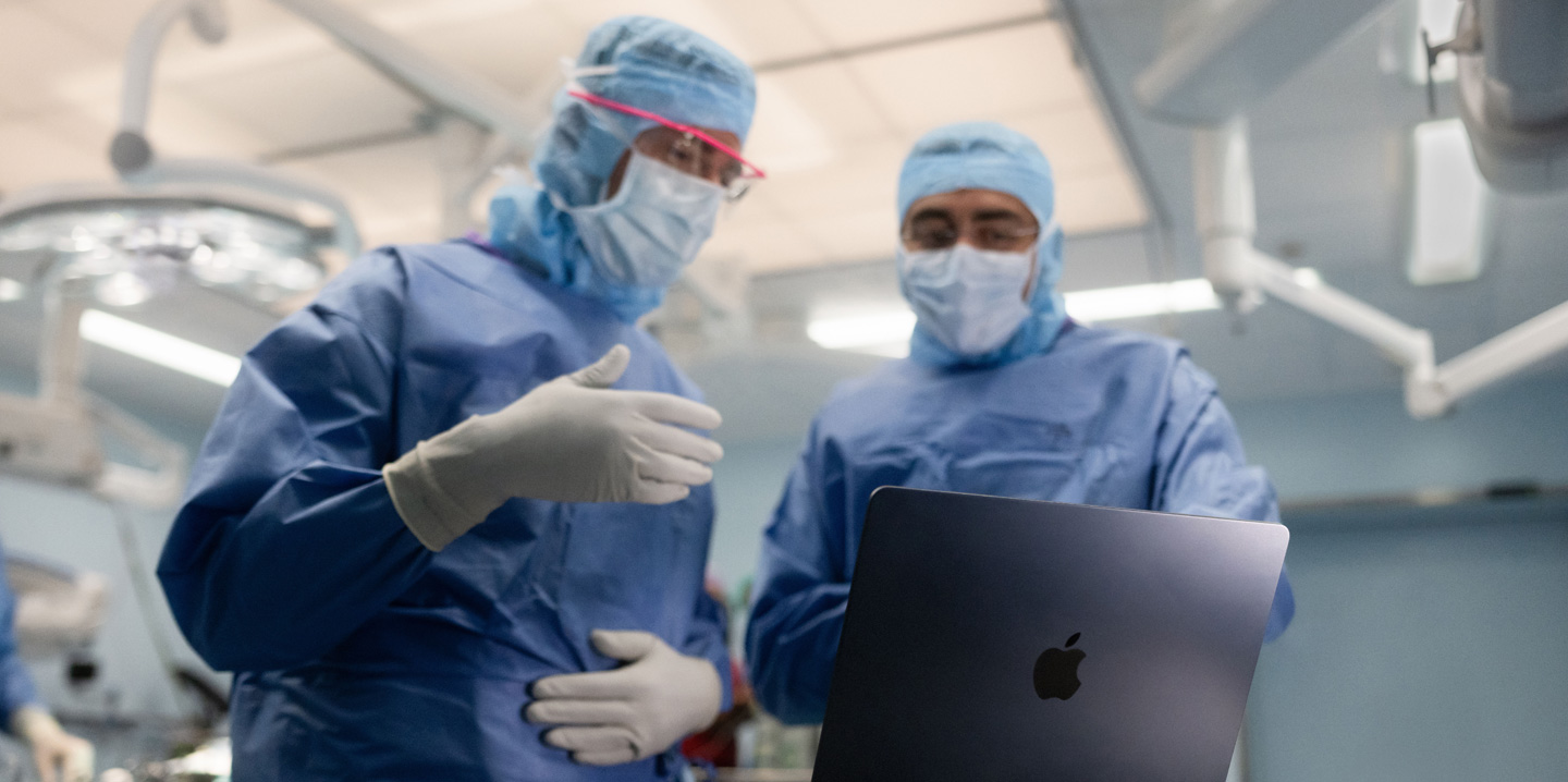 Twee chirurgen in de operatiekamer kijken naar een MacBook, de één gebaart met zijn hand terwijl de ander observeert