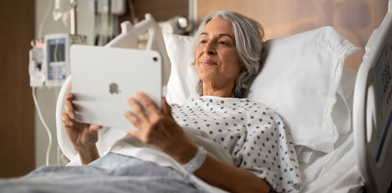 Uma paciente deitada na cama do hospital observando seu iPad.