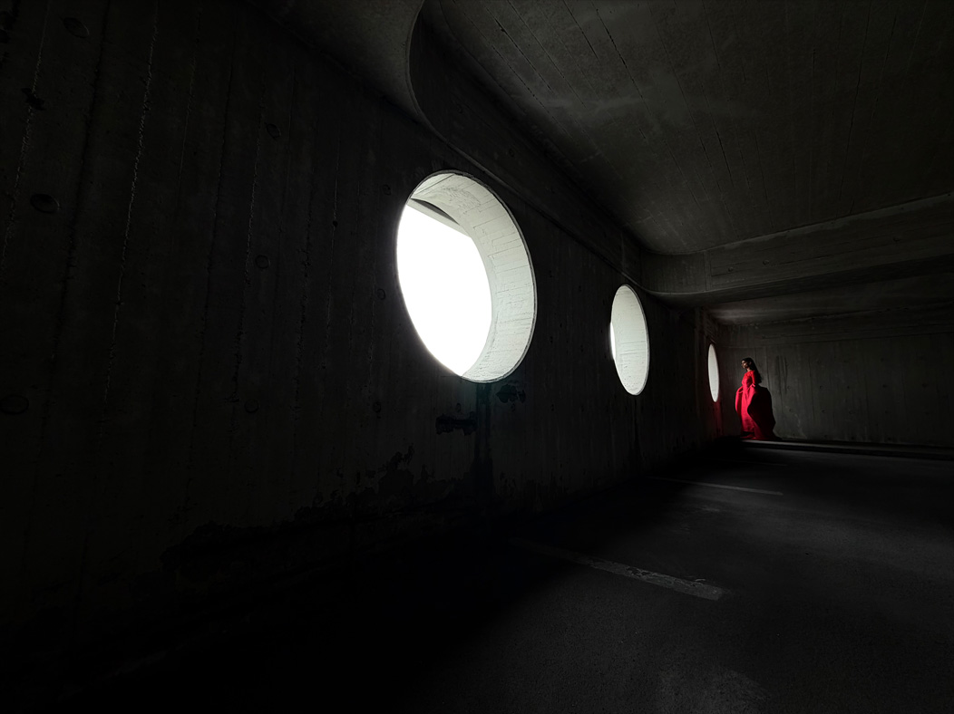 Kobieta w długiej czerwonej sukni stoi w pustym pokoju i jest fotografowana. Apka Zdjęcia prezentuje różne ogniskowe, od 200 mm do 13 mm, demonstrując możliwości systemu pro aparatów