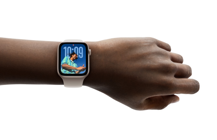 Close-up of Apple Watch in Rose Gold with rubber strap on a person’s wrist, showing Time app in new Liquid Glass design